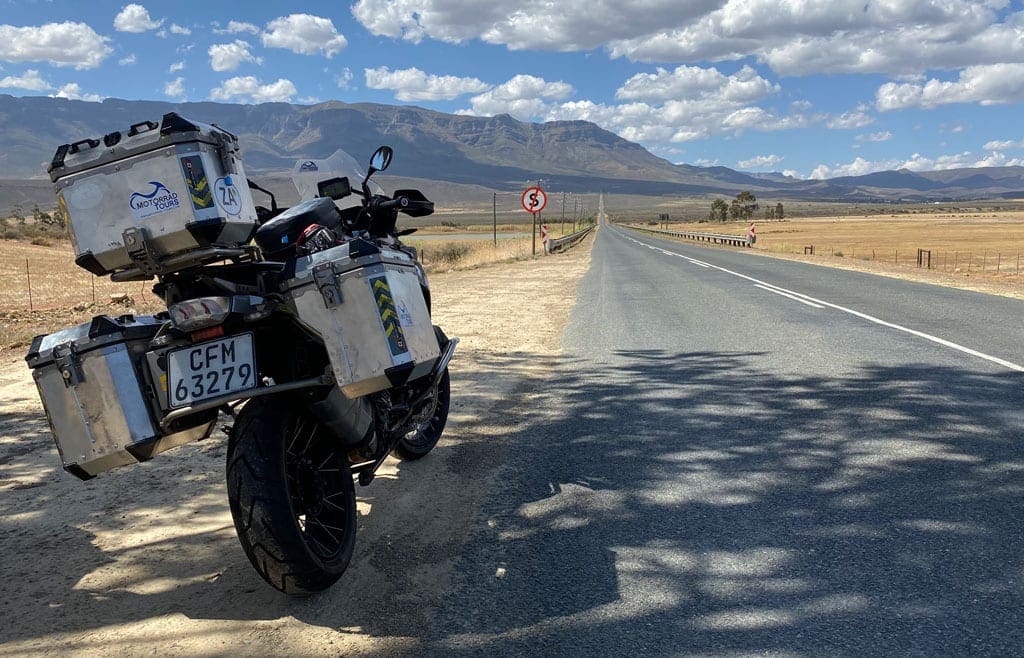 Leaving the city 1 Motorbike parked along the side of a road the goes into the distance.